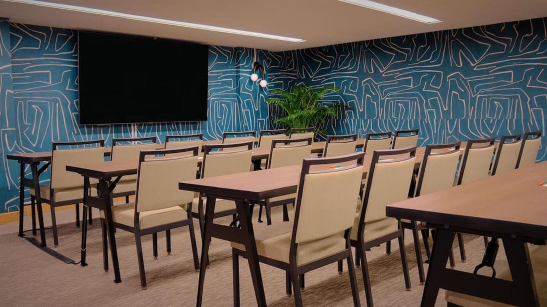 Conference room with rows of tables, chairs, and wall-mounted screen at The Ambassador Hotel Of Waikiki.