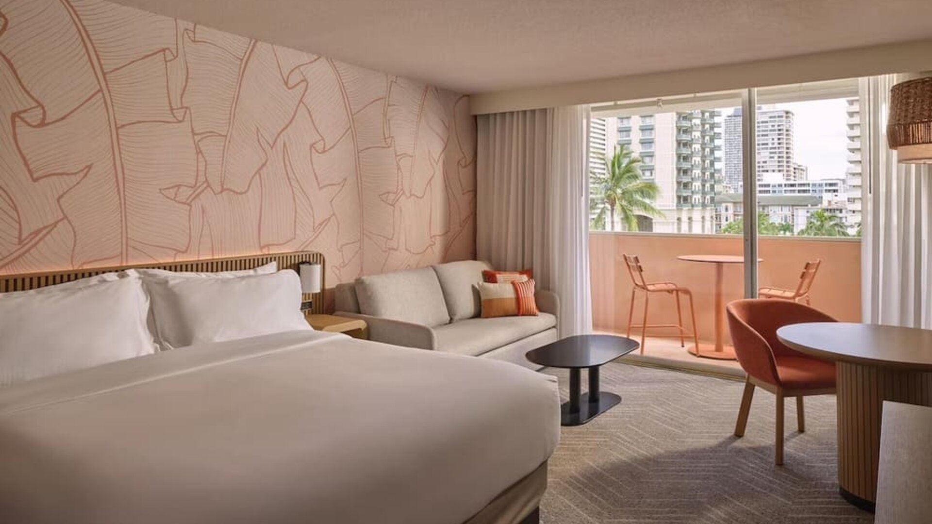 Guest room with bed, sofa seating area, and balcony access with city view at The Ambassador Hotel Of Waikiki.