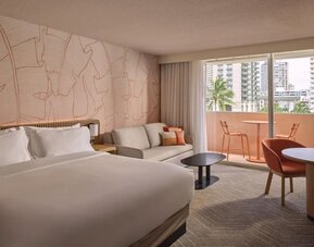 Guest room with bed, sofa seating area, and balcony access with city view at The Ambassador Hotel Of Waikiki.