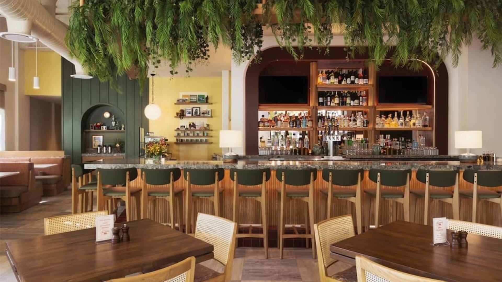 Dining area with bar seating, wooden tables, and hanging greenery decor at The Ambassador Hotel Of Waikiki.