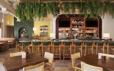 Dining area with bar seating, wooden tables, and hanging greenery decor at The Ambassador Hotel Of Waikiki.
