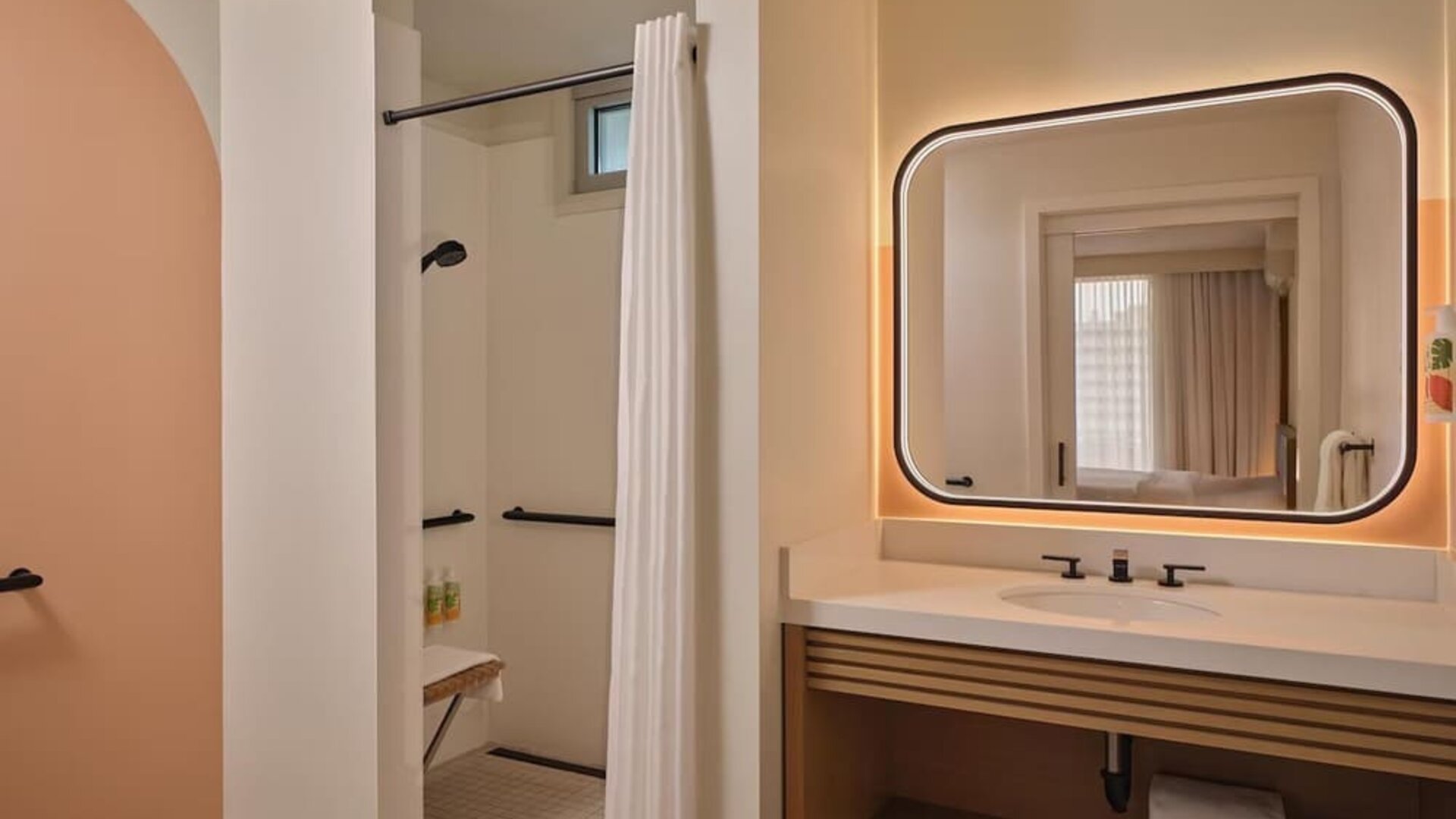 Accessible bathroom with walk-in shower, grab rails, and illuminated mirror at The Ambassador Hotel Of Waikiki.