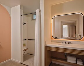 Accessible bathroom with walk-in shower, grab rails, and illuminated mirror at The Ambassador Hotel Of Waikiki.