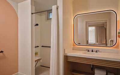 Accessible bathroom with walk-in shower, grab rails, and illuminated mirror at The Ambassador Hotel Of Waikiki.