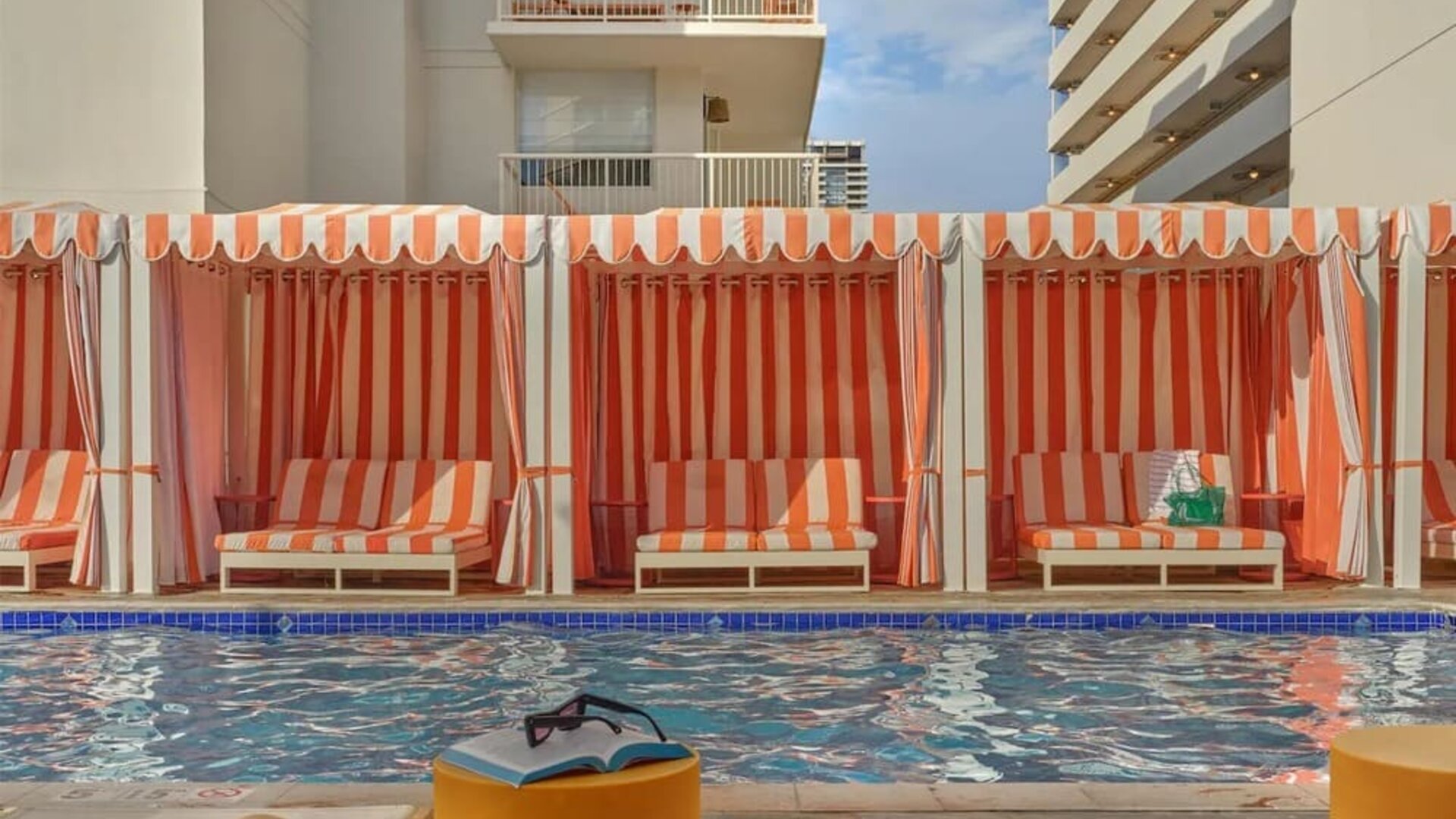Poolside cabanas with striped fabric and lounge seating at The Ambassador Hotel Of Waikiki.