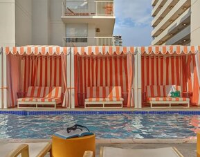 Poolside cabanas with striped fabric and lounge seating at The Ambassador Hotel Of Waikiki.