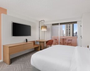 Guest room with balcony, seating area, and TV console at The Ambassador Hotel Of Waikiki.