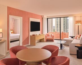 Spacious suite with dining table, lounge seating, and balcony access with city views at The Ambassador Hotel Of Waikiki.