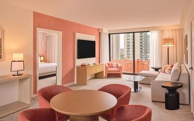 Spacious suite with dining table, lounge seating, and balcony access with city views at The Ambassador Hotel Of Waikiki.
