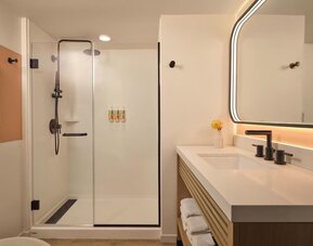 Modern bathroom with walk-in glass shower, vanity, and illuminated mirror at The Ambassador Hotel Of Waikiki.