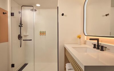 Modern bathroom with walk-in glass shower, vanity, and illuminated mirror at The Ambassador Hotel Of Waikiki.
