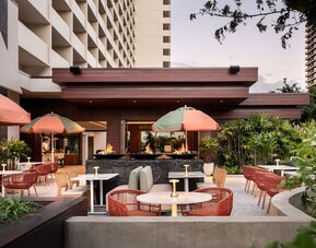 Outdoor patio area with seating, fire features, and landscaped surroundings at The Ambassador Hotel Of Waikiki.