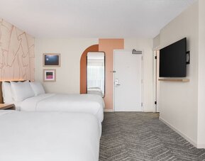 Guest room with two beds, wall-mounted TV, and minimalist decor at The Ambassador Hotel Of Waikiki.