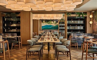Restaurant dining space with long tables, cushioned chairs, wood accents, and decorative ceiling lighting at Romer House Waikiki.
