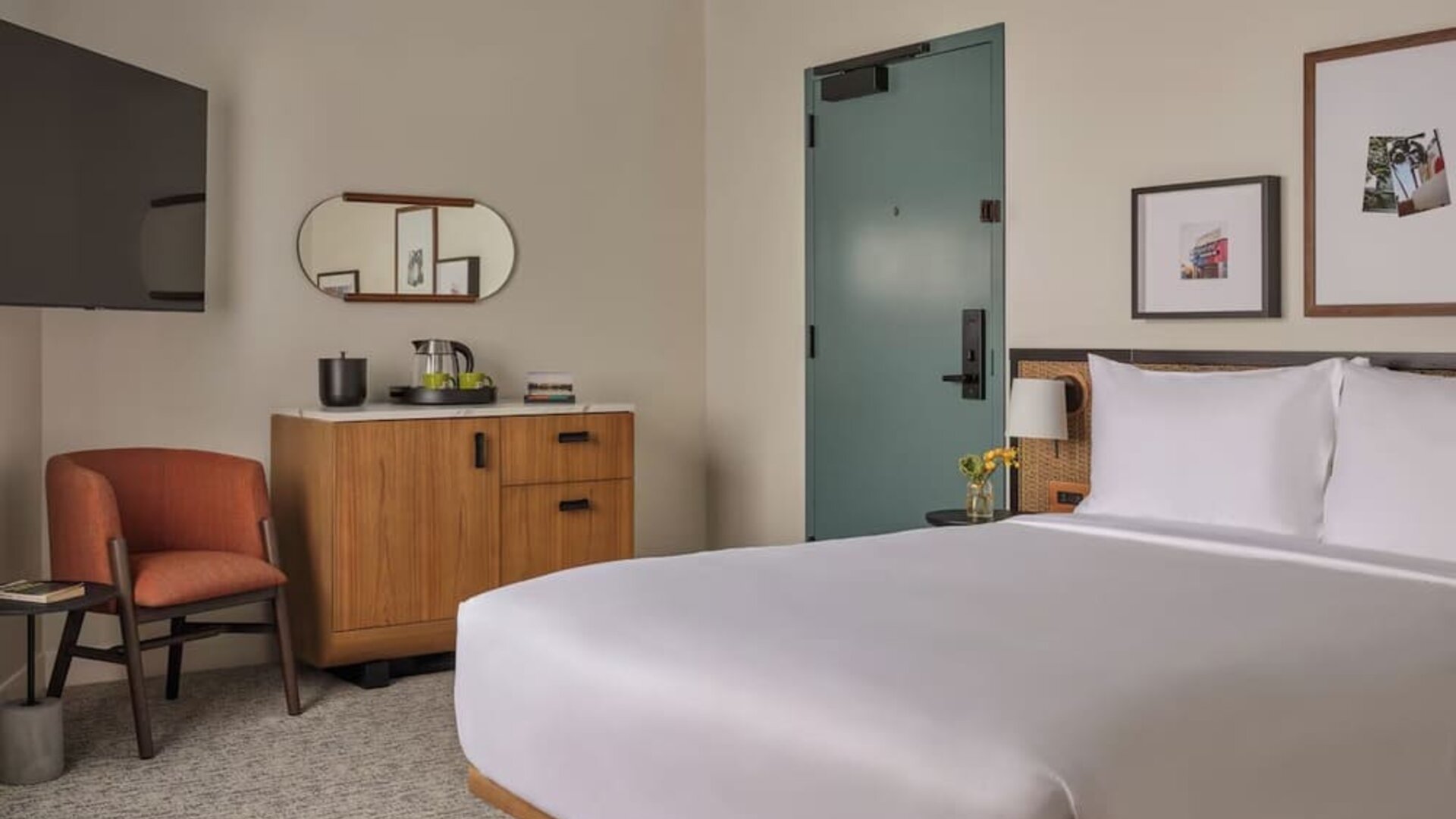 King bed with rattan headboard, bedside lamps, seating nook, and framed artwork in a bright room at Romer House Waikiki.