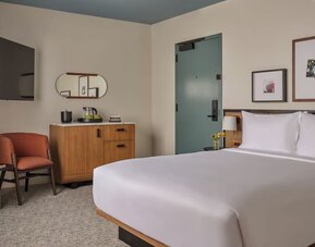 King bed with rattan headboard, bedside lamps, seating nook, and framed artwork in a bright room at Romer House Waikiki.