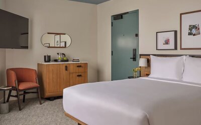 King bed with rattan headboard, bedside lamps, seating nook, and framed artwork in a bright room at Romer House Waikiki.