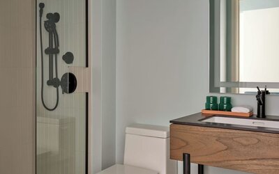 Compact bathroom with glass shower, modern vanity, mirror, and neatly folded towels below sink at Romer House Waikiki.