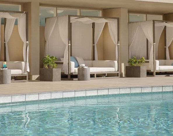Poolside cabanas with white drapes and cushioned loungers beside outdoor pool at The Twin Fin Hotel.