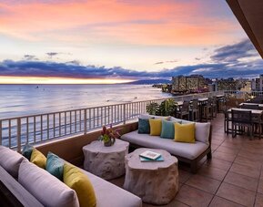 Sunset terrace with lounge seating overlooking ocean and Waikiki skyline at The Twin Fin Hotel.