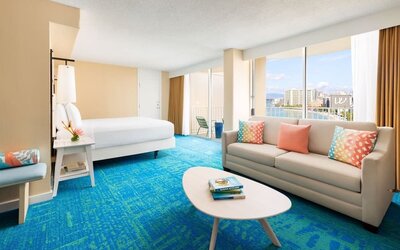 Bright suite with king bed, sofa seating area, colorful pillows, and ocean-facing balcony at The Twin Fin Hotel.