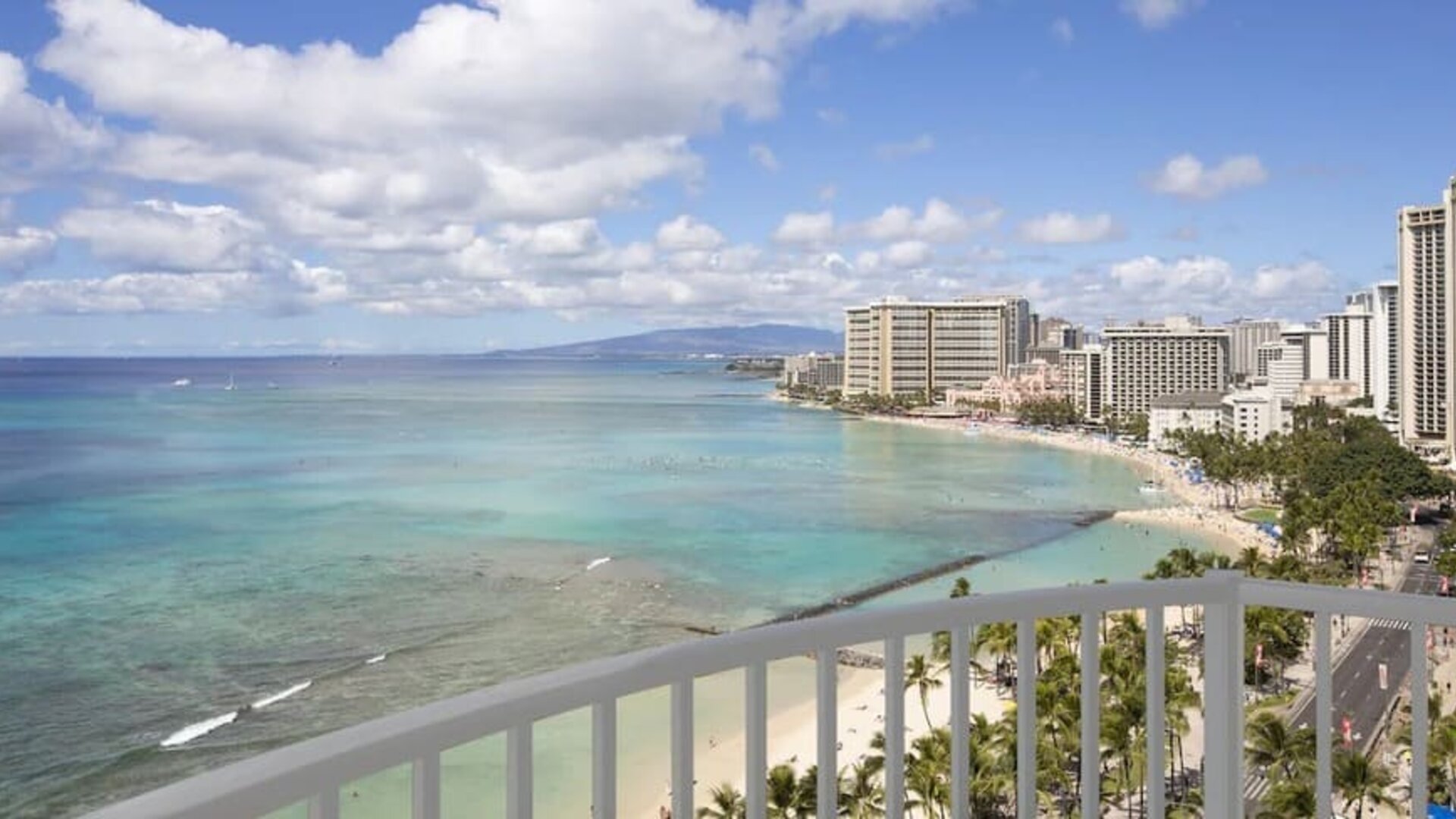 High-rise balcony view overlooking Waikiki Beach, turquoise ocean, and beachfront hotels at The Twin Fin Hotel.