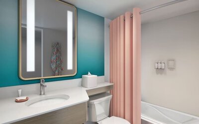 Bathroom with vanity, illuminated mirror, bathtub with pink curtain, and teal accent wall at The Twin Fin Hotel.