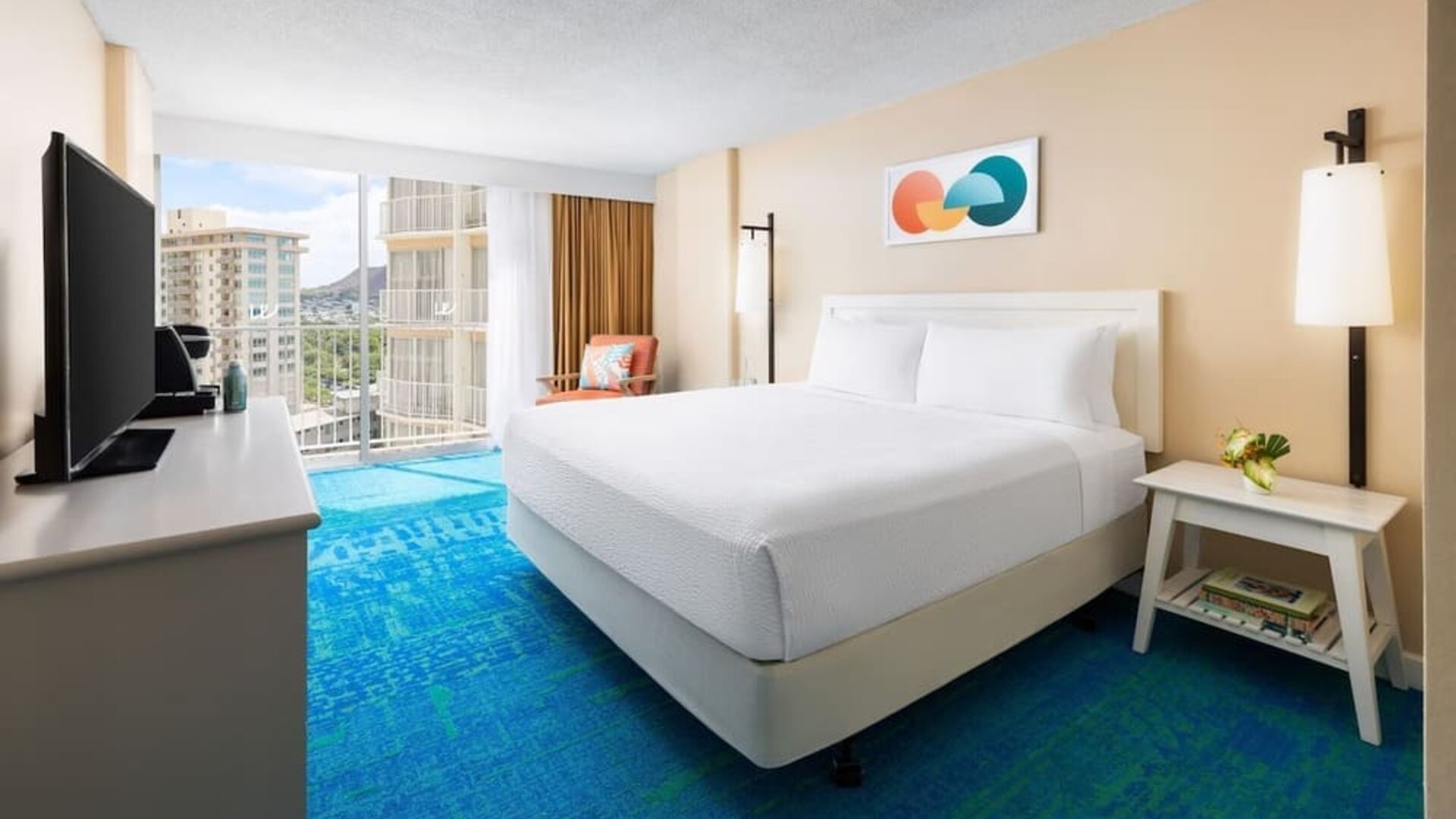 King bed room with balcony view, TV console, and mountain scenery in the distance at The Twin Fin Hotel.