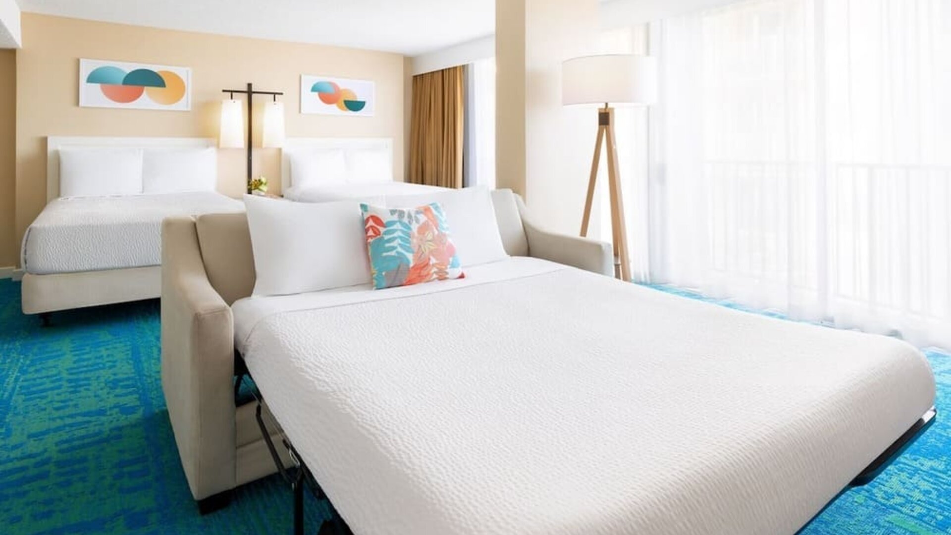 Spacious suite with two beds, sofa bed, and large window with sheer curtains at The Twin Fin Hotel.