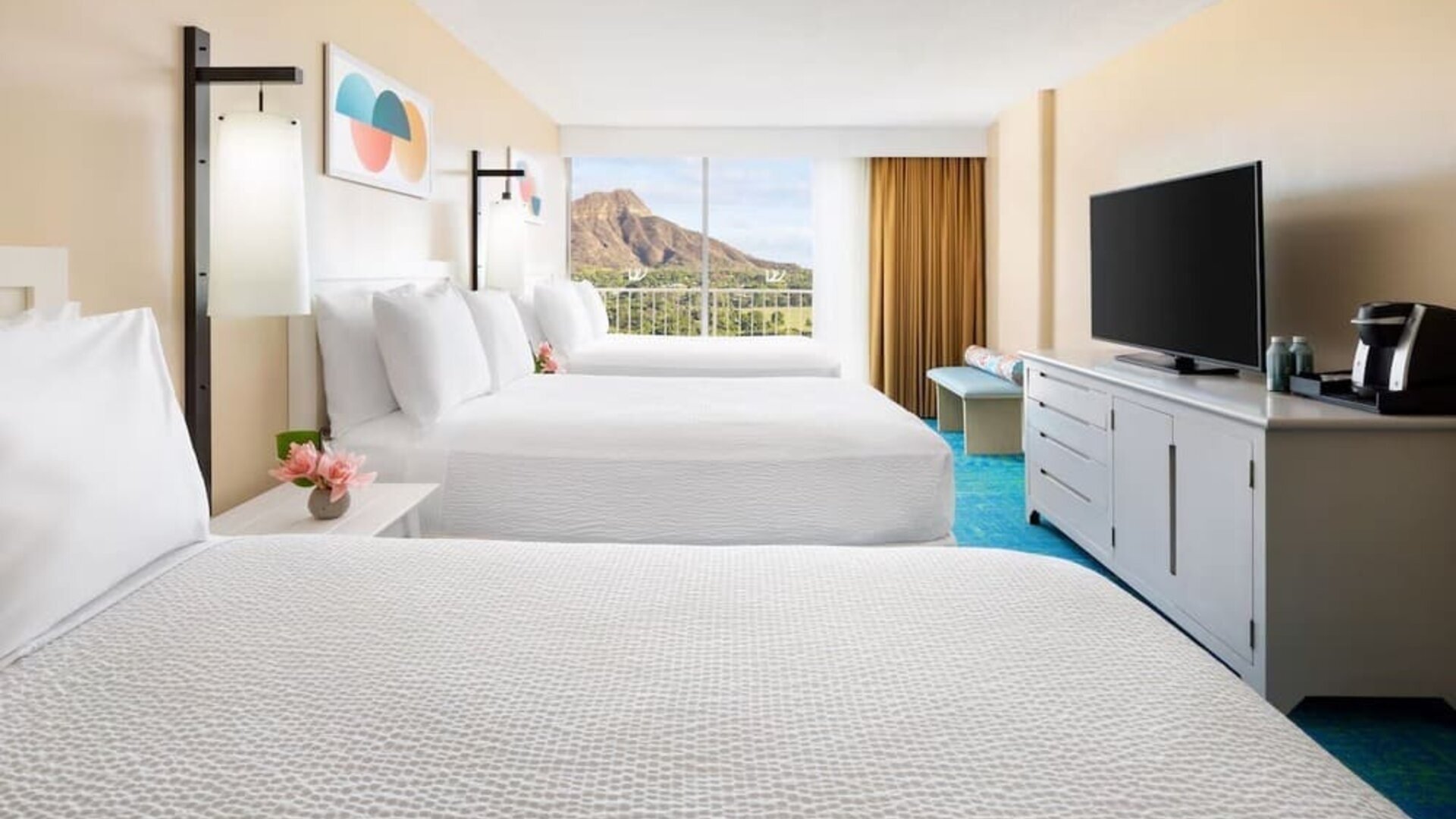 Room with three double beds, TV console, and balcony facing mountain view at The Twin Fin Hotel.