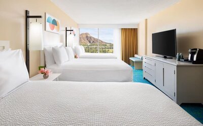 Room with three double beds, TV console, and balcony facing mountain view at The Twin Fin Hotel.