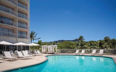Outdoor pool with lounge chairs, umbrellas, and views of surrounding greenery at Park Shore Waikiki.