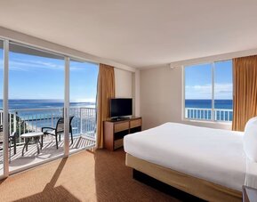 Bright corner room with king bed, large windows, balcony, and sweeping ocean views at Park Shore Waikiki.