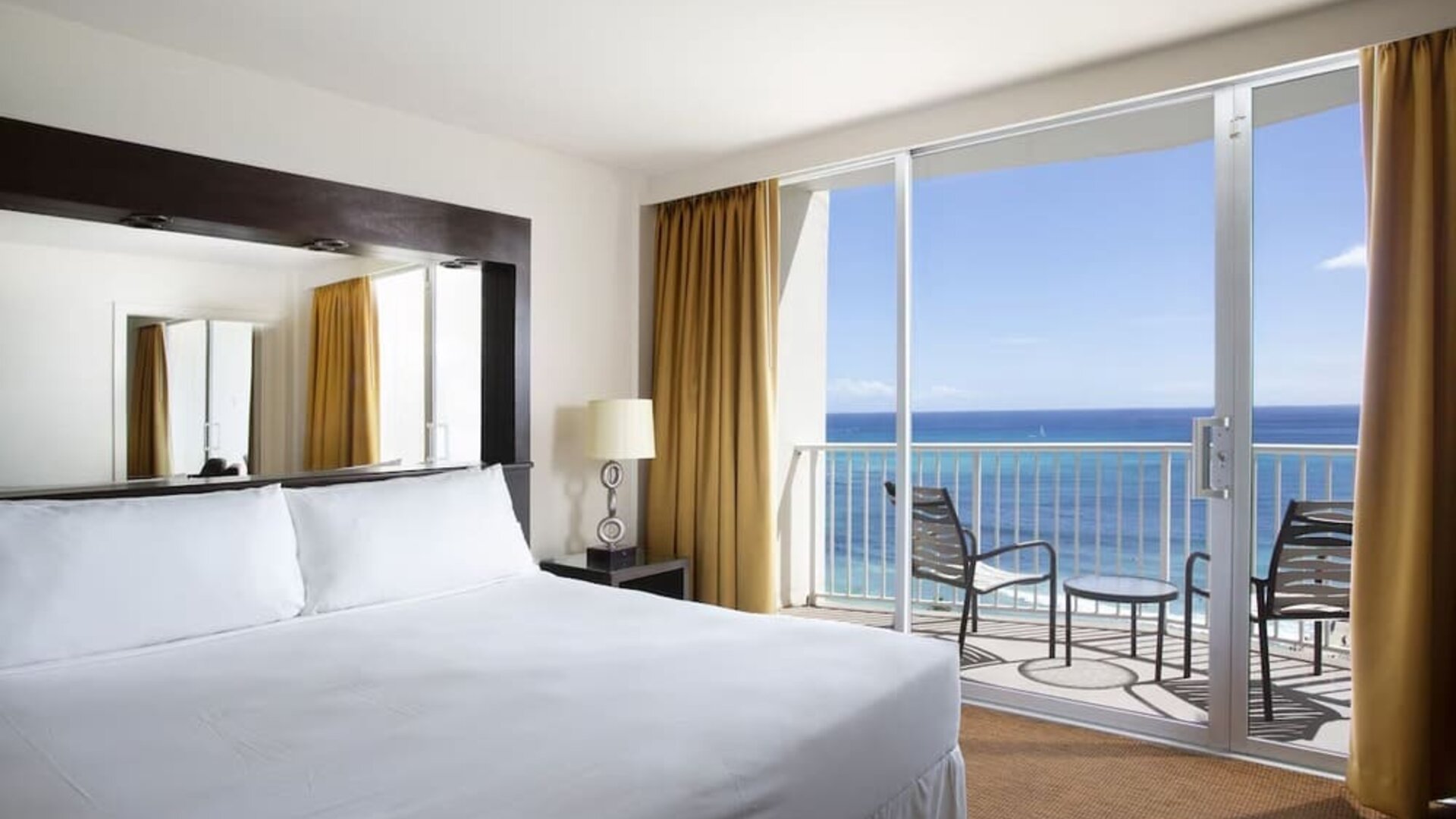 King bed room with oceanfront balcony, floor lamp, and seating area at Park Shore Waikiki.