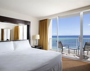 King bed room with oceanfront balcony, floor lamp, and seating area at Park Shore Waikiki.