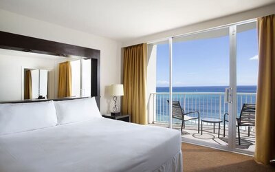 King bed room with oceanfront balcony, floor lamp, and seating area at Park Shore Waikiki.