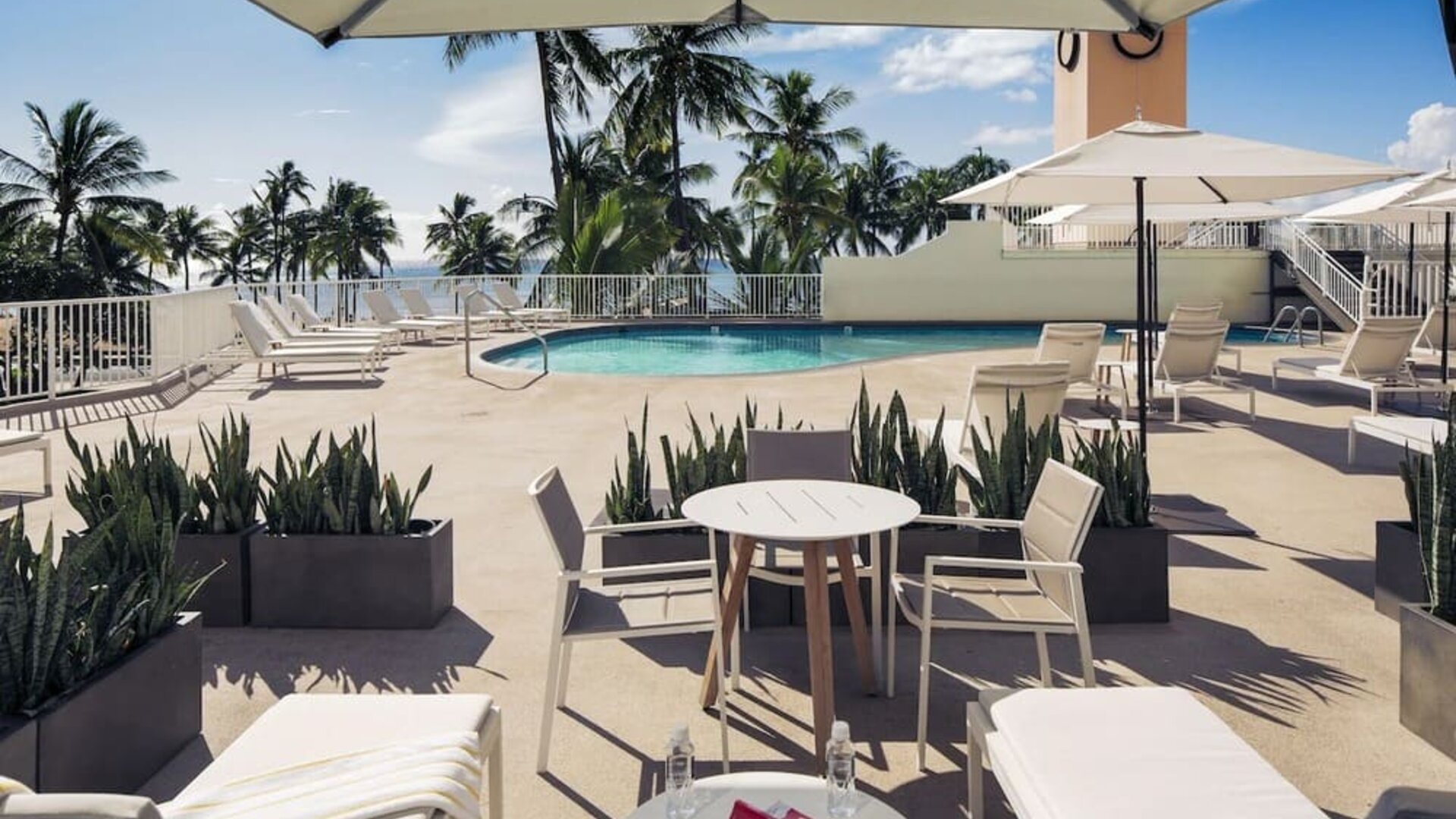 Poolside seating area with tables, loungers, and umbrellas near the outdoor pool at Park Shore Waikiki.