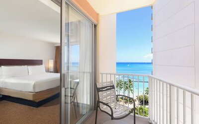 Room with king bed and sliding glass doors leading to a balcony with ocean and pool views at Park Shore Waikiki