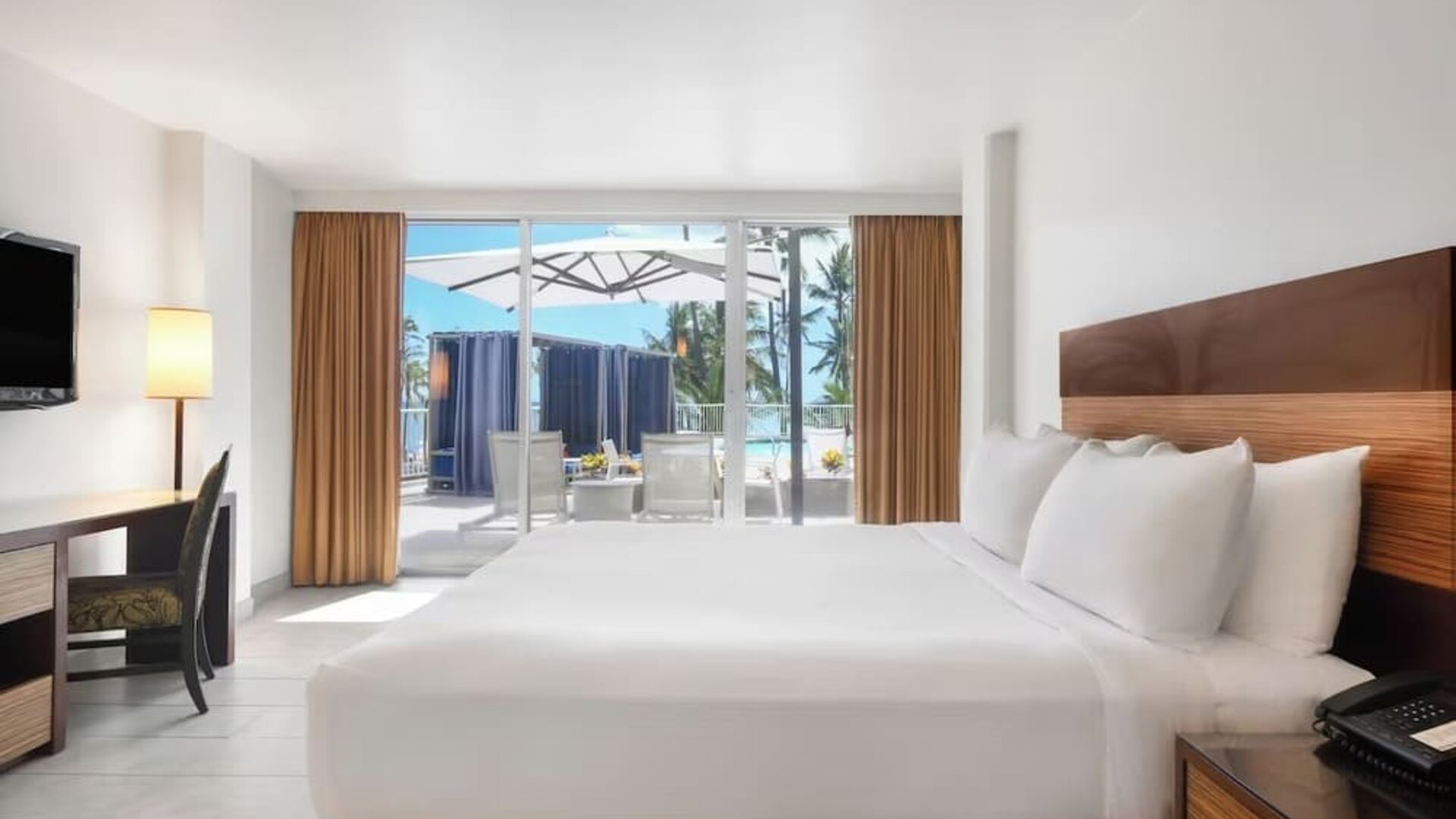King bed room with desk, TV, and sliding doors opening to a patio with seating at Park Shore Waikiki.