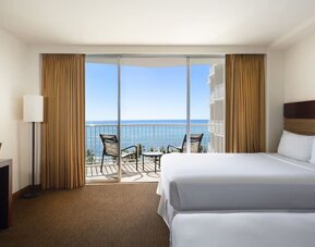 Room with two beds, balcony, and ocean view through sliding glass doors at Park Shore Waikiki.