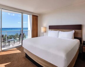 King bed room with ocean-facing balcony, desk, and TV at Park Shore Waikiki.