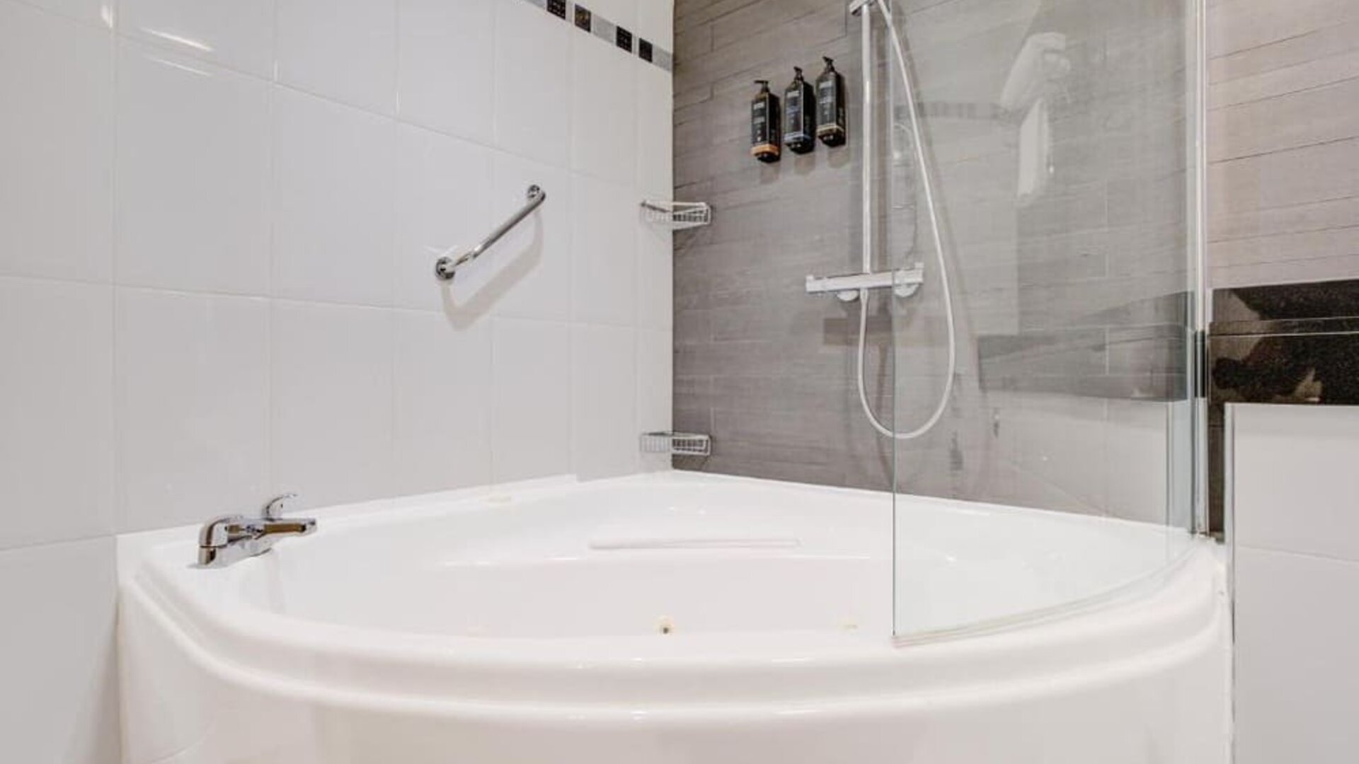 Bathroom with curved bathtub, glass shower screen, and mounted toiletries at Atlantic Tower Hotel Liverpool By Sunday.