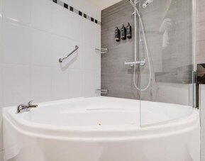 Bathroom with curved bathtub, glass shower screen, and mounted toiletries at Atlantic Tower Hotel Liverpool By Sunday.