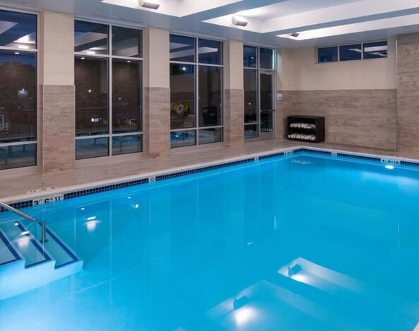 Indoor pool with large windows, entry steps, and poolside seating at Holiday Inn & Suites Farmington Hills - Detroit NW By IHG.