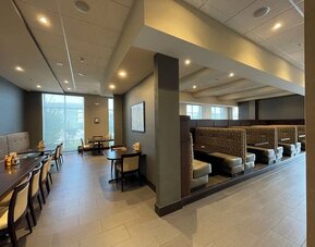 Dining area with booth seating, tables, and warm lighting at Holiday Inn & Suites Farmington Hills - Detroit NW By IHG.