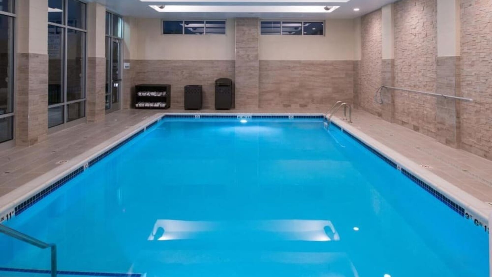 Indoor swimming pool with steps, tiled walls, and ceiling lights at Holiday Inn & Suites Farmington Hills - Detroit NW By IHG.
