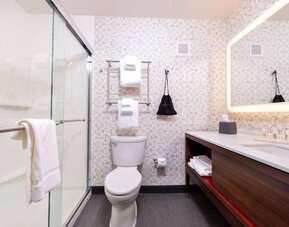 Bathroom with walk-in shower, toilet, towels, and illuminated mirror at Holiday Inn & Suites Farmington Hills - Detroit NW By IHG.