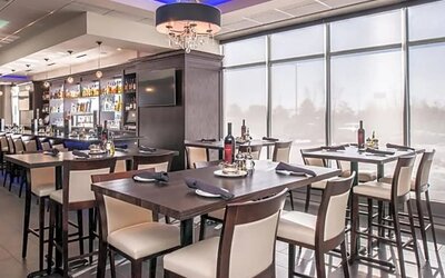Restaurant dining area with tables, chairs, bar counter, and large windows at Holiday Inn & Suites Farmington Hills - Detroit NW By IHG.
