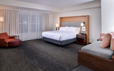 Large suite with king bed, sofa seating, and wide window with sheer curtains at Holiday Inn & Suites Farmington Hills - Detroit NW By IHG.