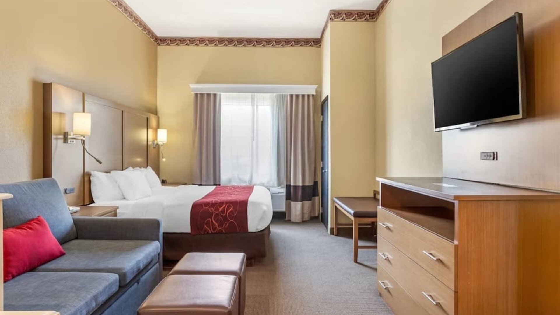 Guest room with king bed, sofa seating, ottoman, dresser, and wall-mounted TV at Comfort Suites Bush Intercontinental Airport.